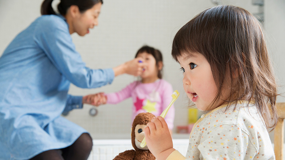 Two little girls and a mother is helping one of them eating; image used for HSBC Helper Insurance.