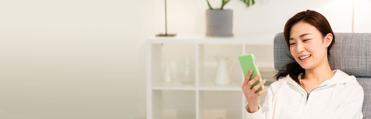 A woman is leaning on a sofa and using a smart phone ; image used in HSBC Broking's mobile trading page.